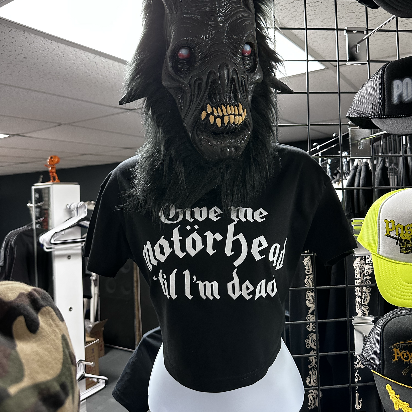 Person wearing a black t-shirt with text and a dark mask in a store setting