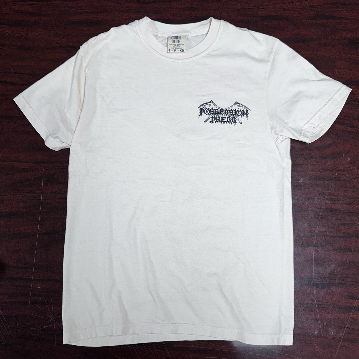 Ivory t-shirt with a black 'Possession Press' logo on a wooden surface