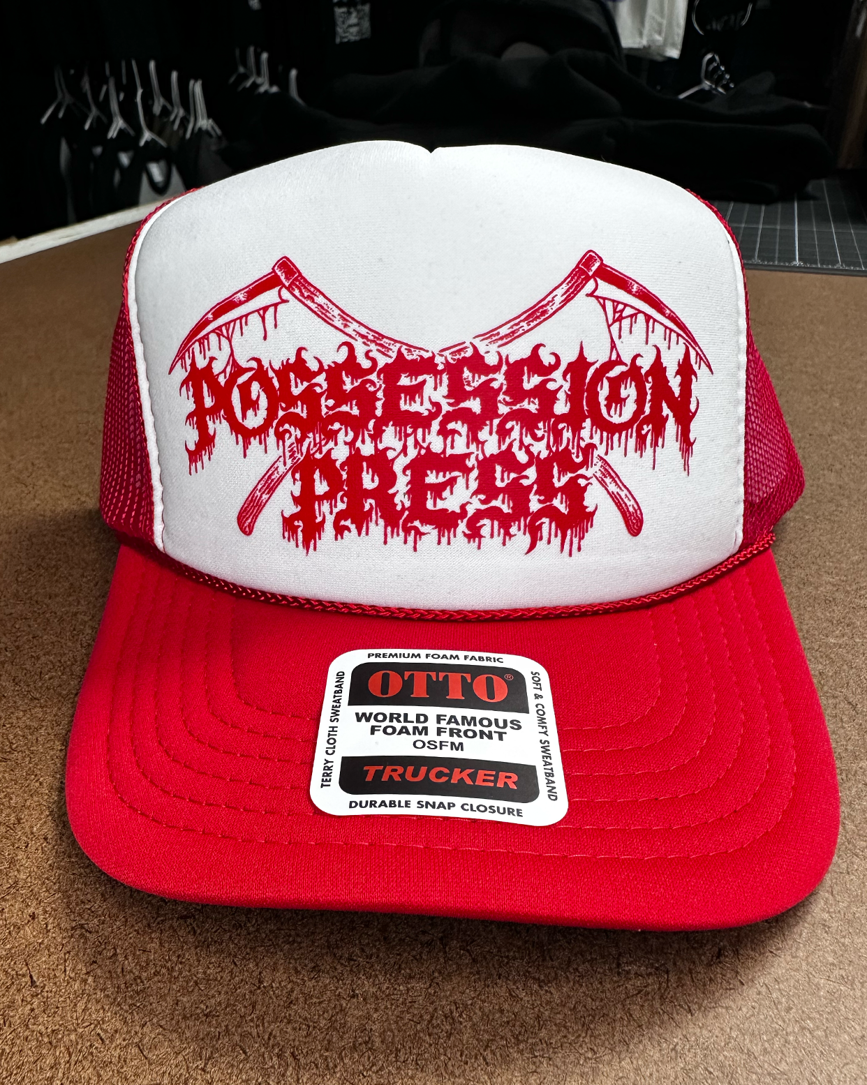 Red and white trucker hat with red Possession Press logo and Otto label on a brown surface.