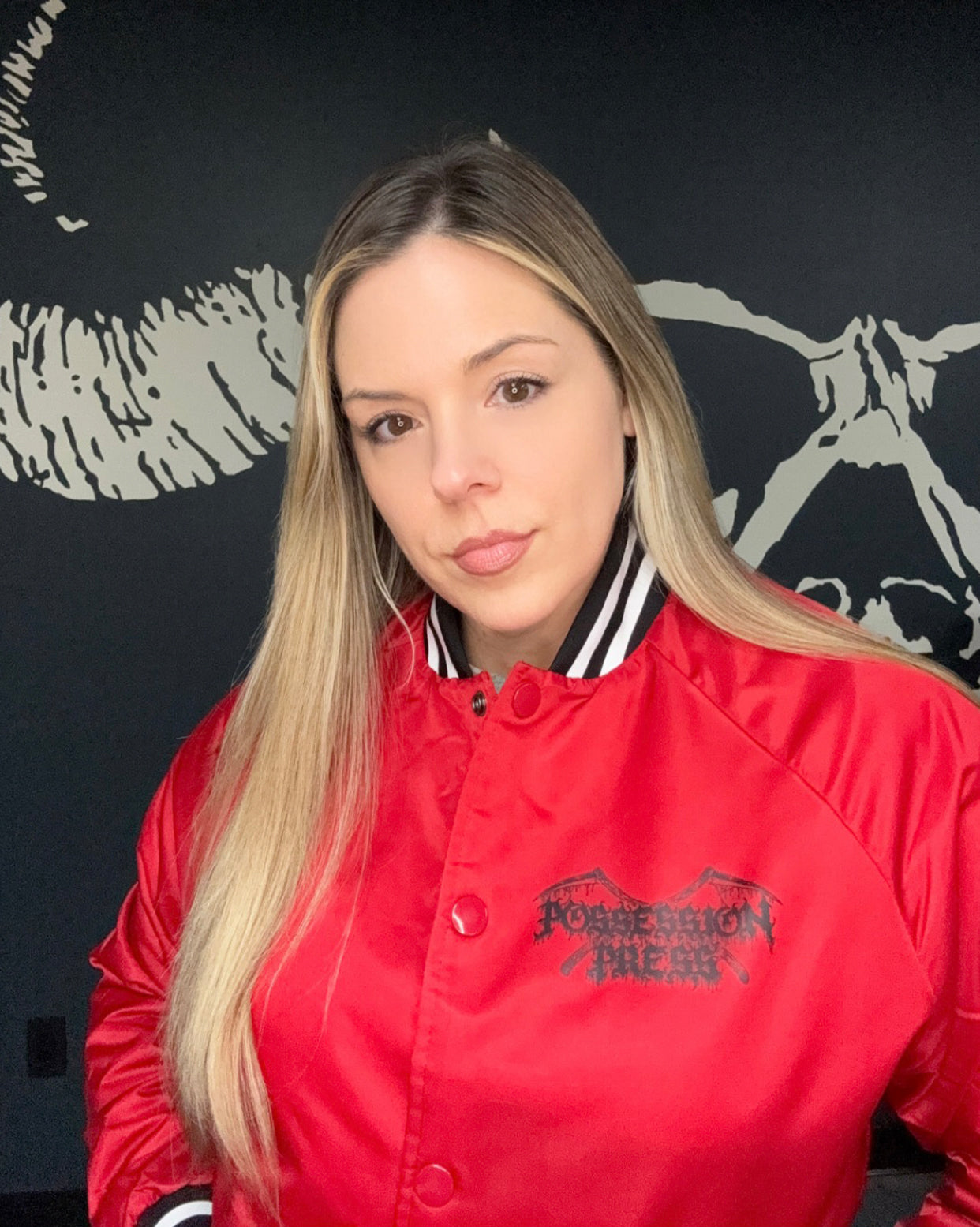 Woman wearing a red jacket with a black Possession Press logo against a dark background with white graphics
