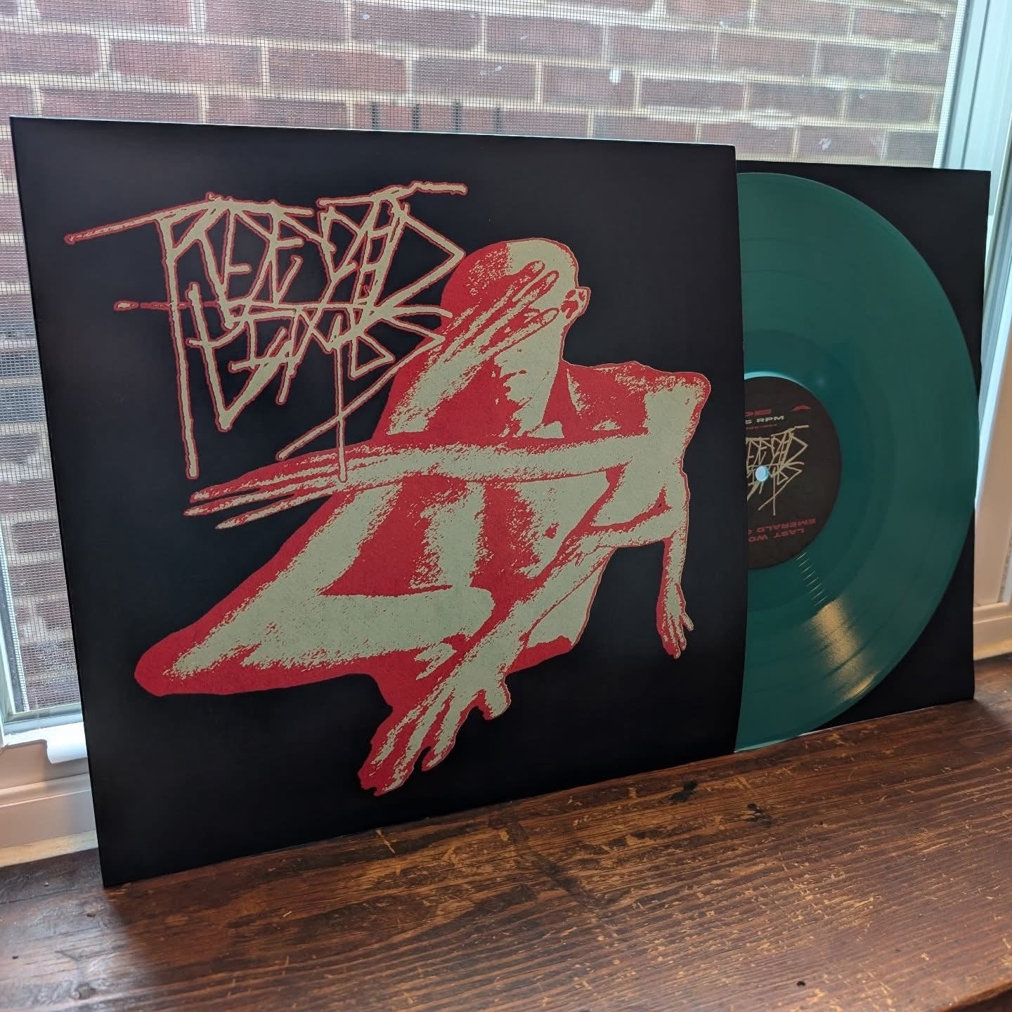 Vinyl record with a black cover featuring a red and white illustration of a person and a geometric design, on a wooden surface.