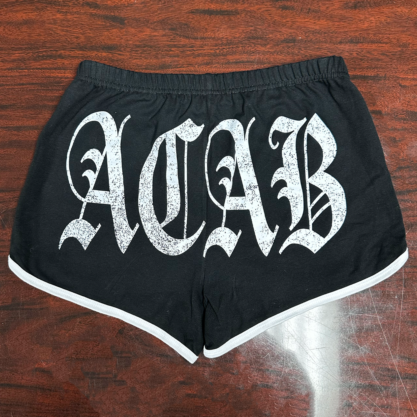 Black shorts with 'ACAB' text on a wooden surface