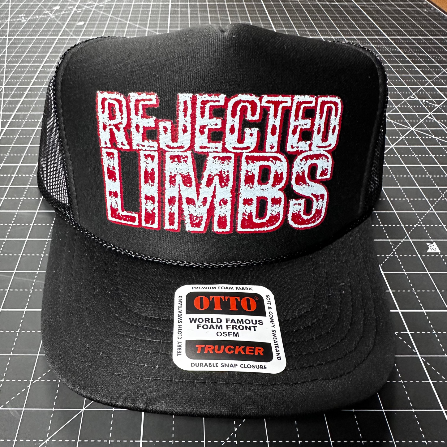 Black trucker hat with 'Rejected Limbs' text on a cutting mat