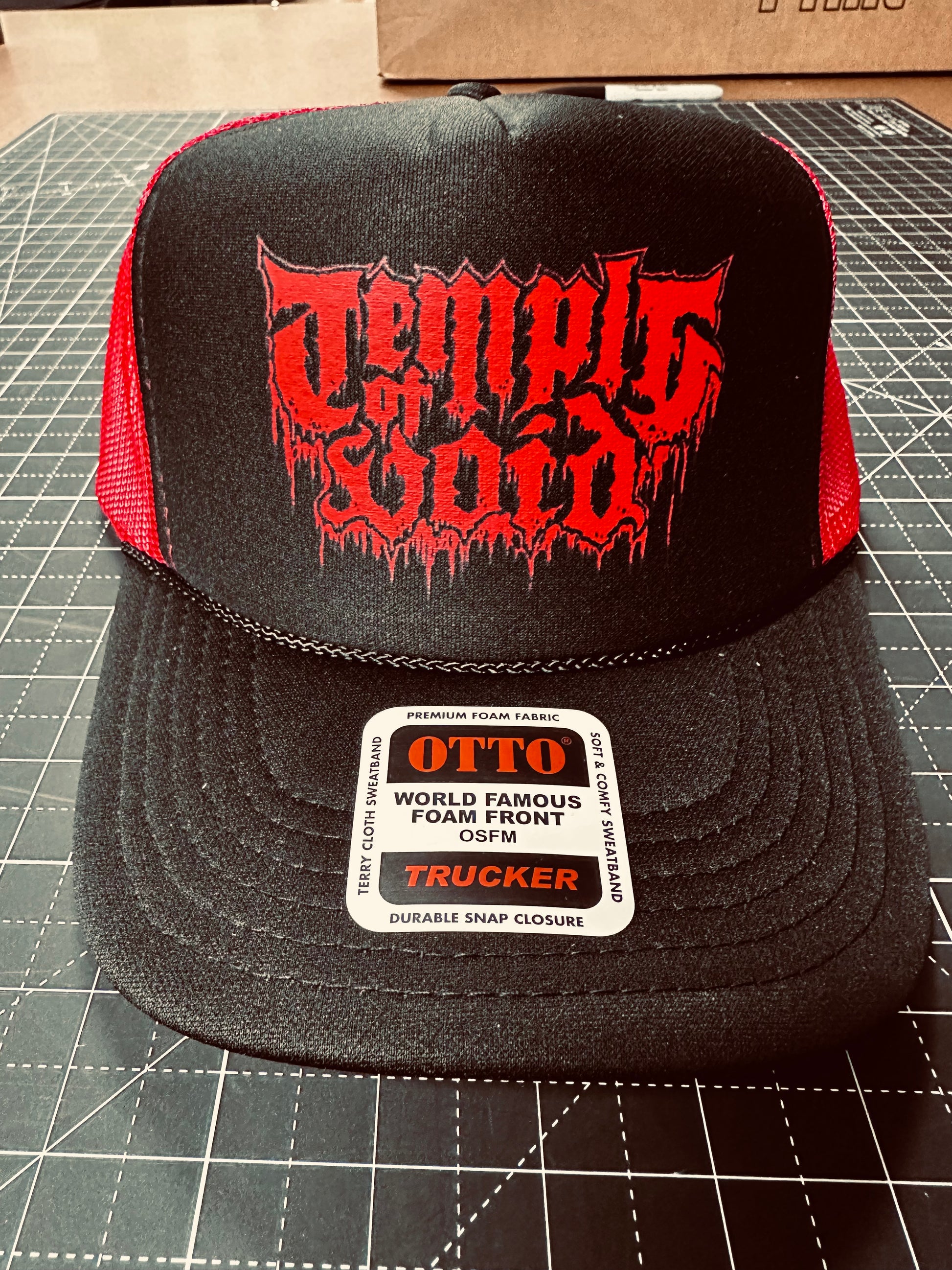 Black and red trucker hat with 'Temple of Void logo on a cutting mat.