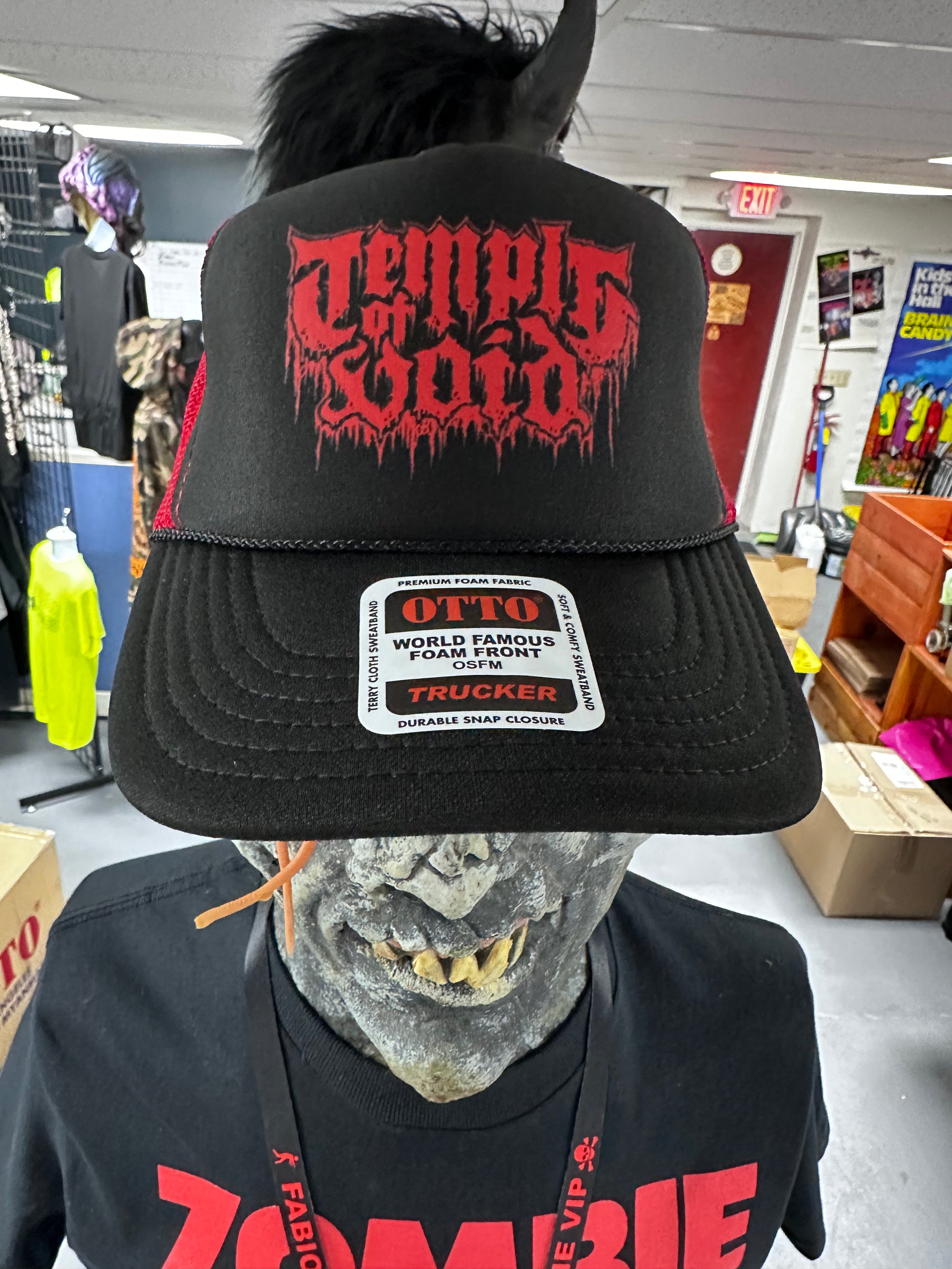 Person wearing a black cap with red text and a zombie mask in a store setting
