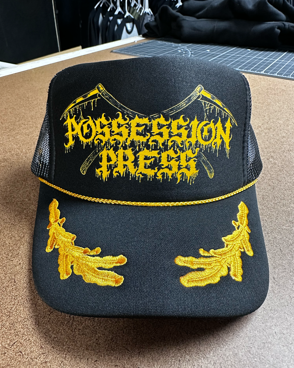Black and gold laurel trucker hat with Possession Press logo in gold