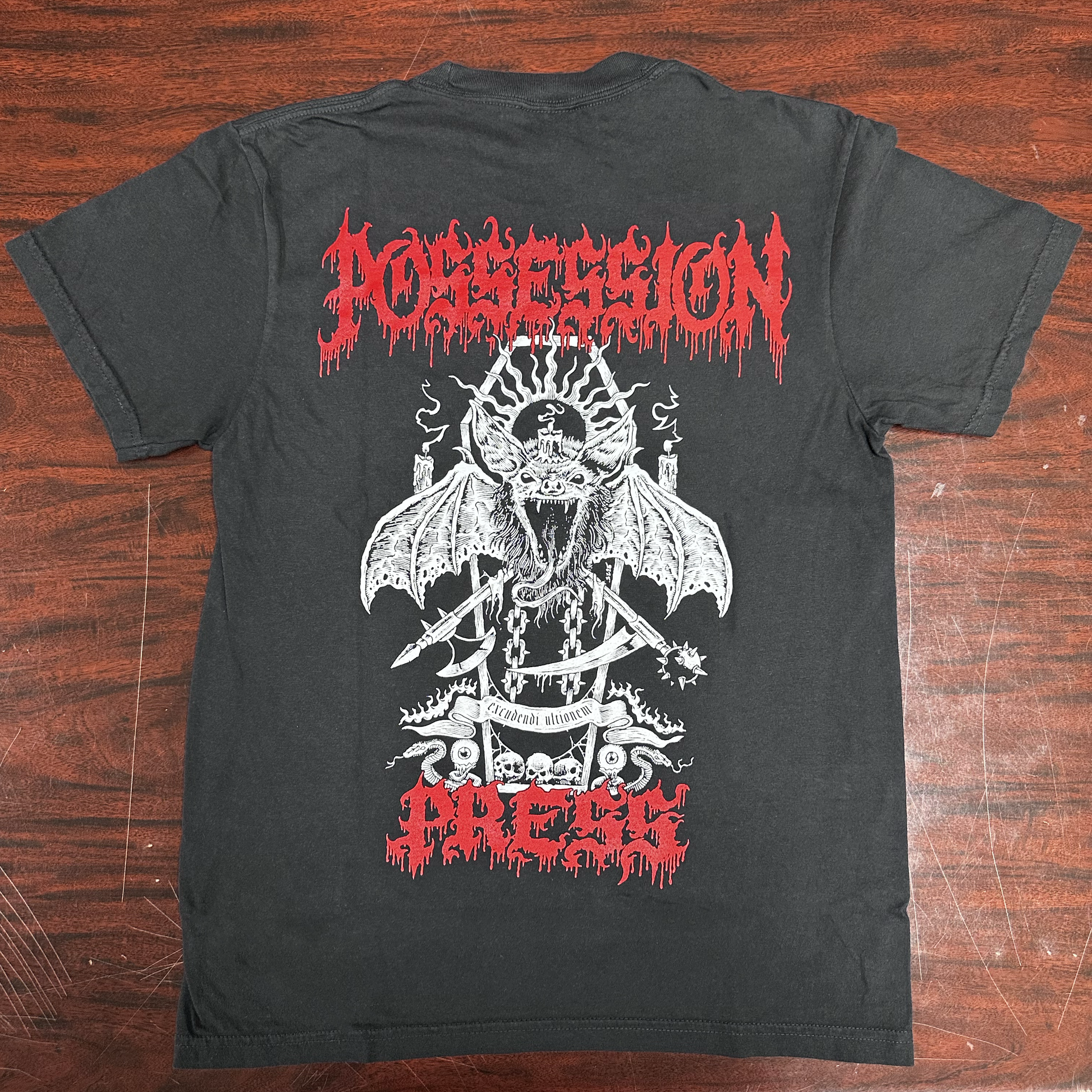 Black t-shirt with red and white graphic design of a coffin bat on a wooden surface