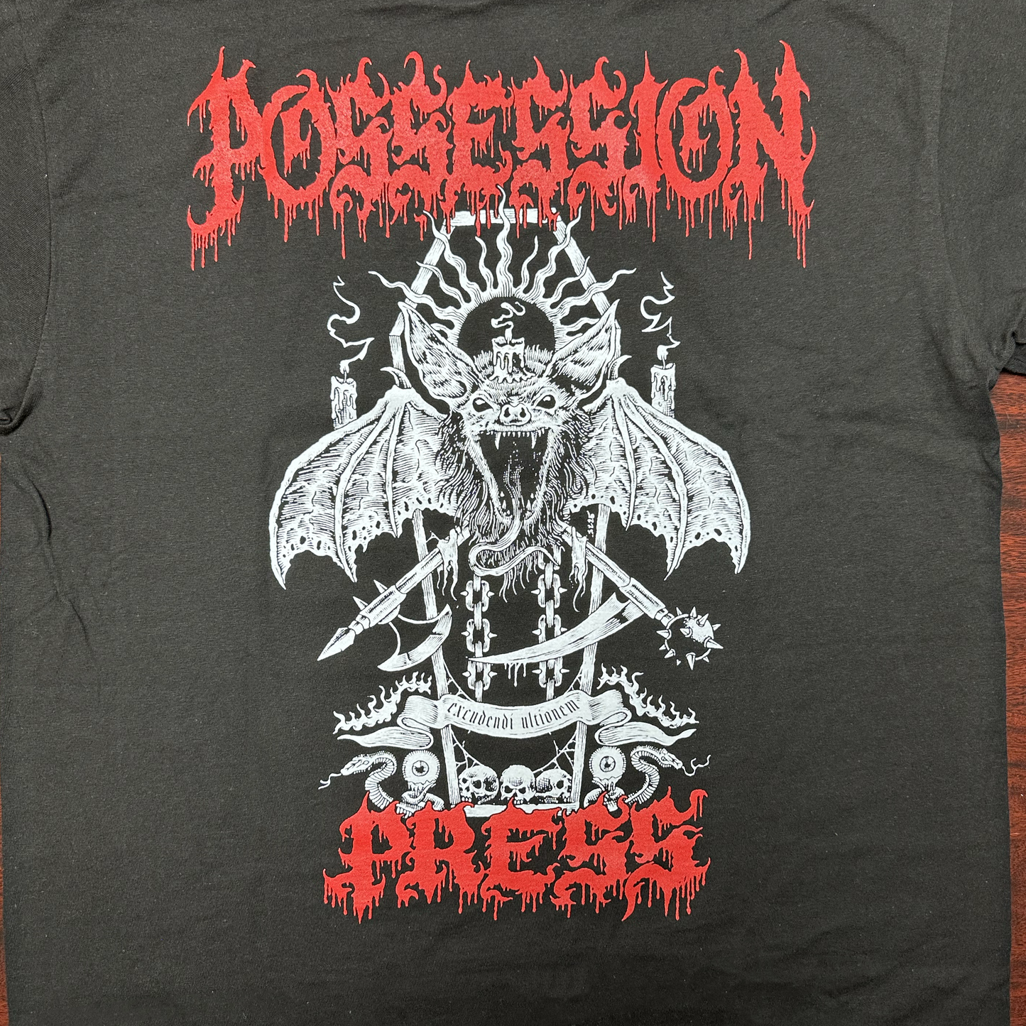 Black t-shirt with white graphic design featuring a bat-like creature and red 'Possession Press' text on a wooden surface.