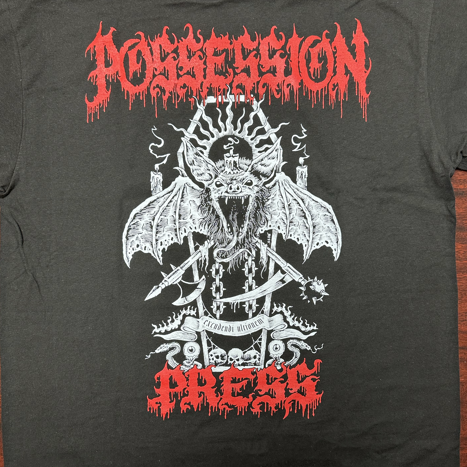 Black t-shirt with white graphic design featuring a bat-like creature and red 'Possession Press' text on a wooden surface.