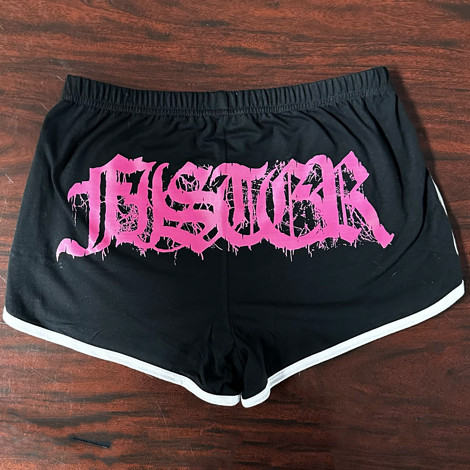 Black shorts with pink "Fister" text on a wooden surface