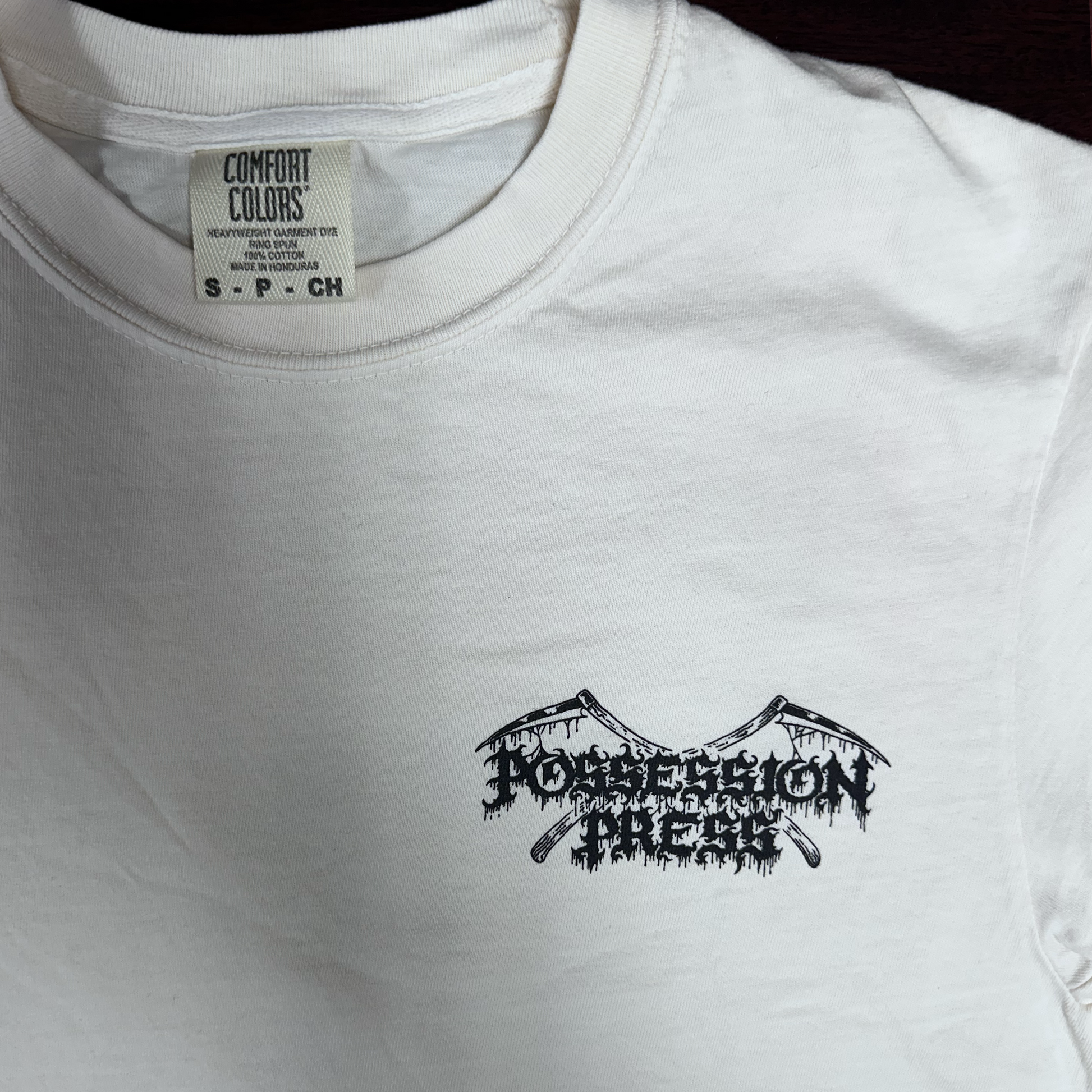 Ivory t-shirt with black graphic design and 'Comfort Colors' label on a dark surface