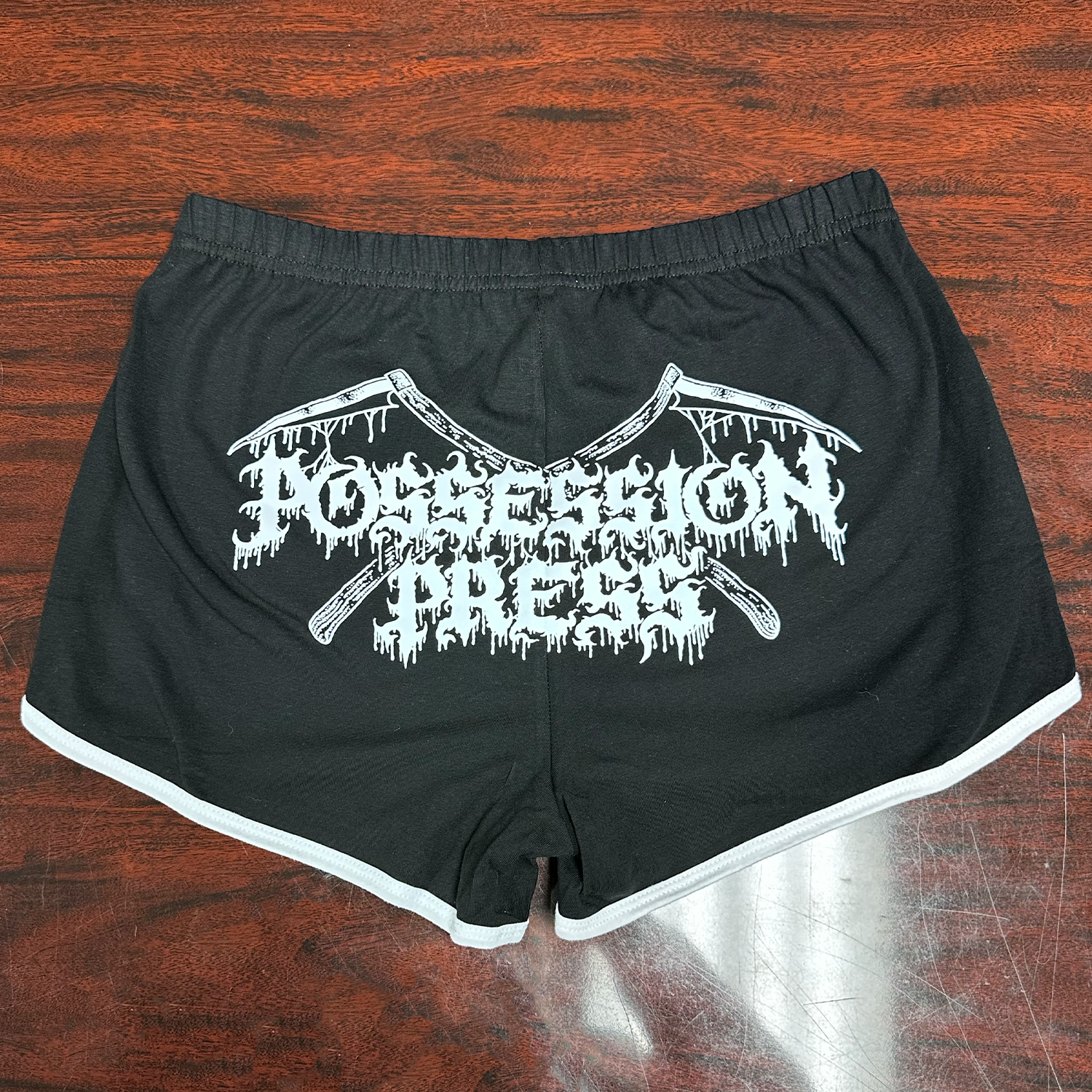 Black shorts with white Possession Press logo on a wooden surface