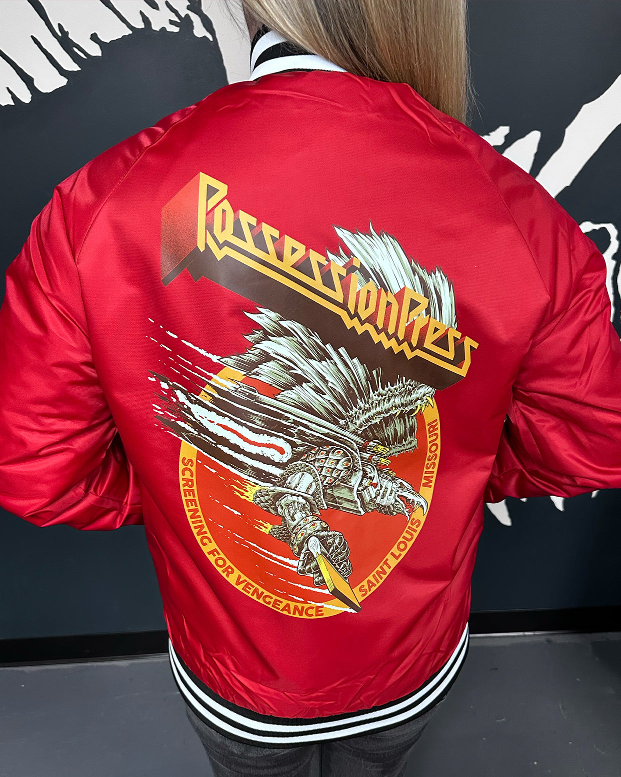 Red jacket with an eagle design and Possession Press text on the back, worn by a person.